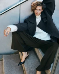 Model wearing dark trousers and heavy coat on outdoor concrete stairs for H&M