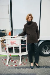 Model wearing a brown turtleneck sweater and black leather trousers standing by a production truck