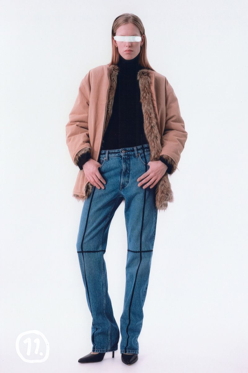 Fashion model poses in a fur-trimmed jacket, blue jeans, and high heels against a white backdrop in a studio fashion editorial.