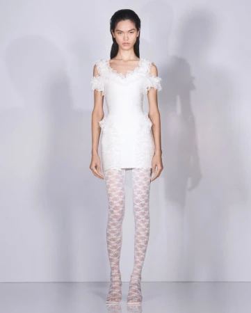 Full-length studio shot of a slender Asian woman wearing a short white lace dress and patterned white tights against a gradient white background.