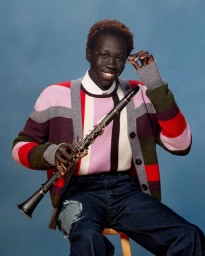 Portrait of a Black man with short red hair wearing a striped cardigan and glasses holding a clarinet