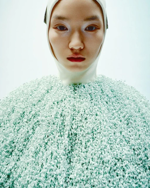 Portrait of an East Asian fashion model wearing a unique light green textured dress and white head covering in a photo studio.