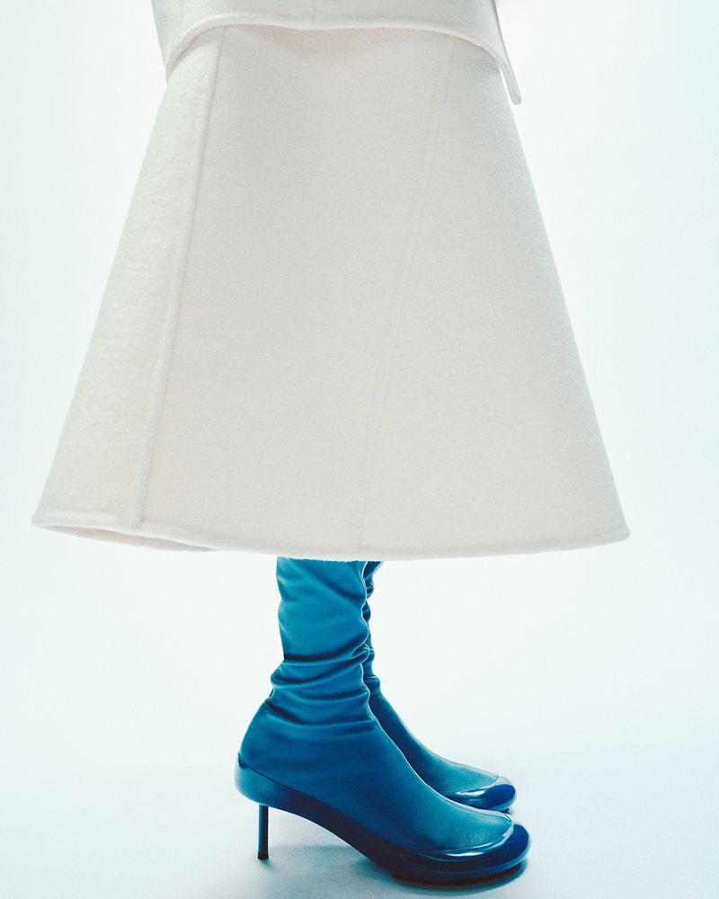 Fashion shot of woman wearing a white dress with blue high heel boots against a white backdrop in a studio setting.