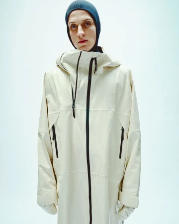 Model wearing a hooded cream zip jacket and dark balaclava against a bright white background