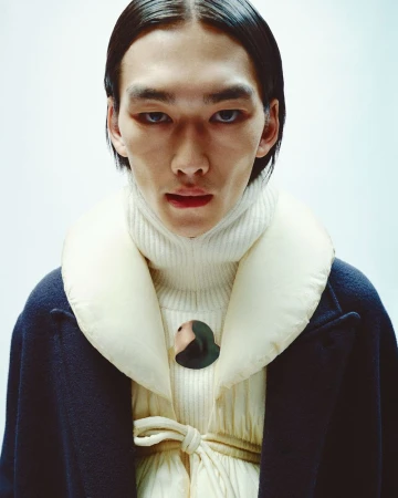 Close-up of an Asian adult male in a cream turtleneck, a blue overcoat with a cream puffy collar and dark hair, set against a pale backdrop.