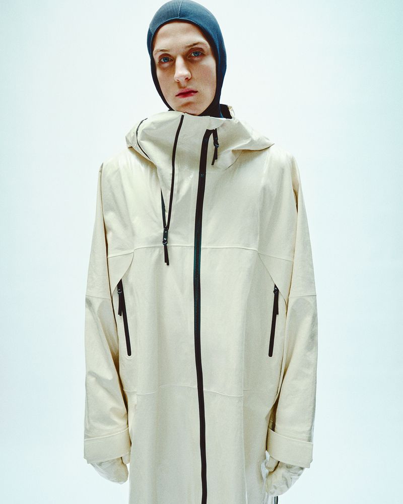 Model wearing a hooded cream zip jacket and dark balaclava against a bright white background