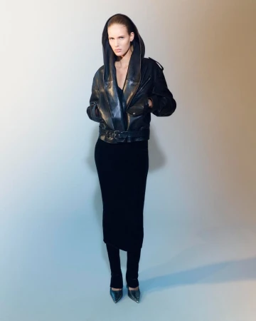 Model wearing a black hooded leather jacket and matching skirt against a gradient backdrop for Mytheresa x Alaia