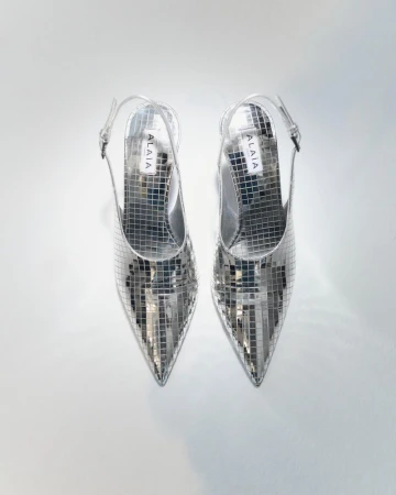 Pair of silver, pointed-toe, slingback heels, made of small reflective squares, arranged on a white background in a studio shot.