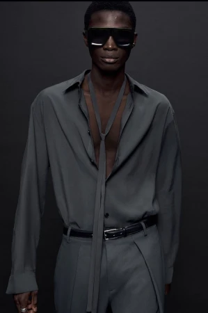 Model wearing dark sunglasses and a grey buttoned shirt with a necktie against a dark background