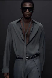 Model wearing dark sunglasses and a grey buttoned shirt with a necktie against a dark background