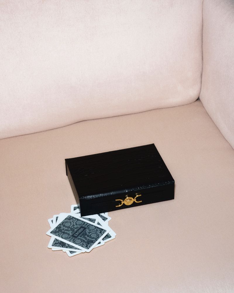 High-angle shot of a black textured box with playing cards on a soft pink surface, possibly a couch or cushion, for an upscale game night.