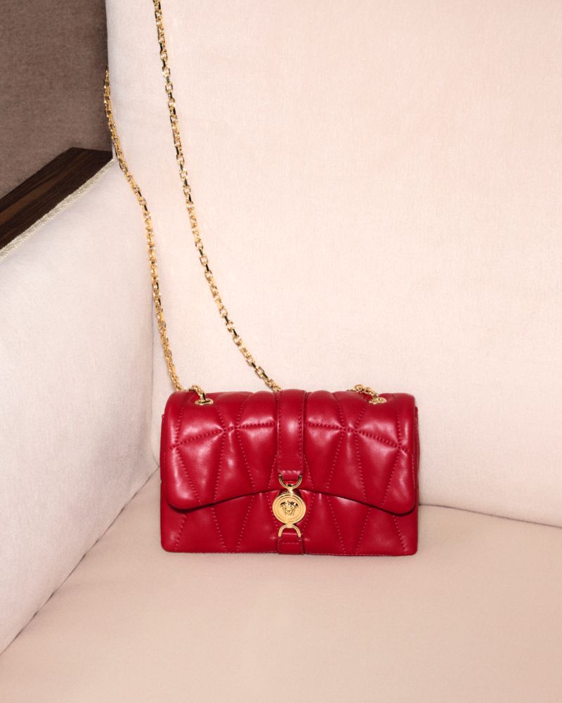 Red quilted leather shoulder bag with a gold chain strap resting on a light cream upholstered sofa surface.