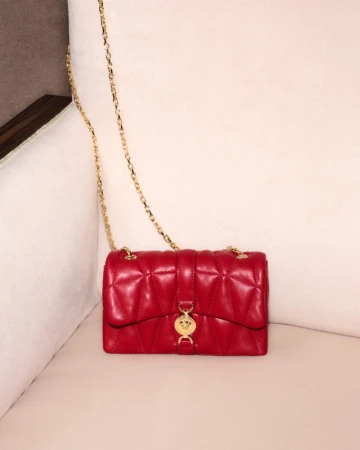 Red quilted leather shoulder bag with a gold chain strap resting on a light cream upholstered sofa surface.