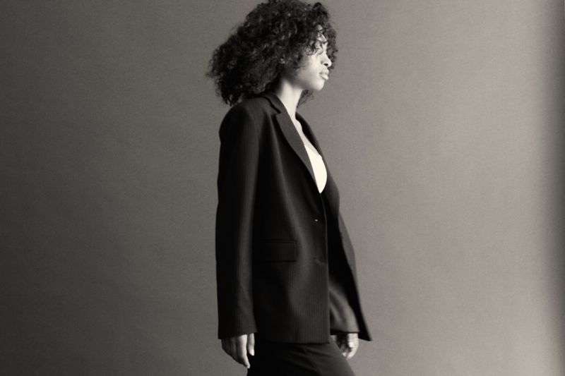 Elegant portrait of a curly-haired woman wearing a black blazer in a photo studio with a neutral backdrop and professional lighting.