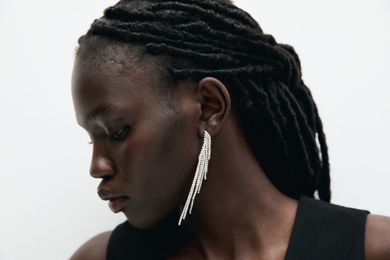 Close-up of a Black woman with locs wearing fringed earrings in a side profile against a white studio background. Fashion beauty shot.