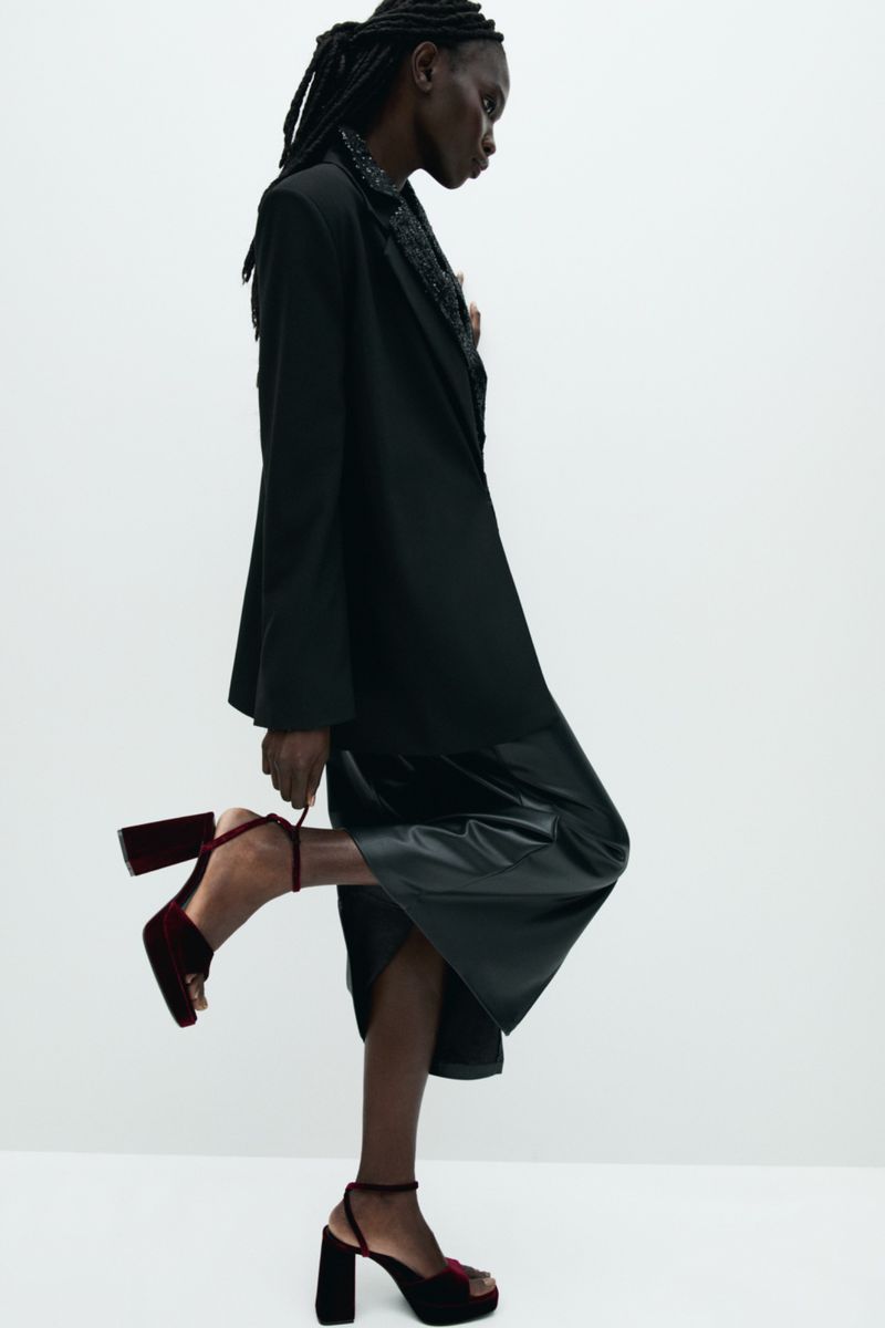 Anok Marial wearing a black blazer and skirt with heeled sandals against a white background for Pull & Bear