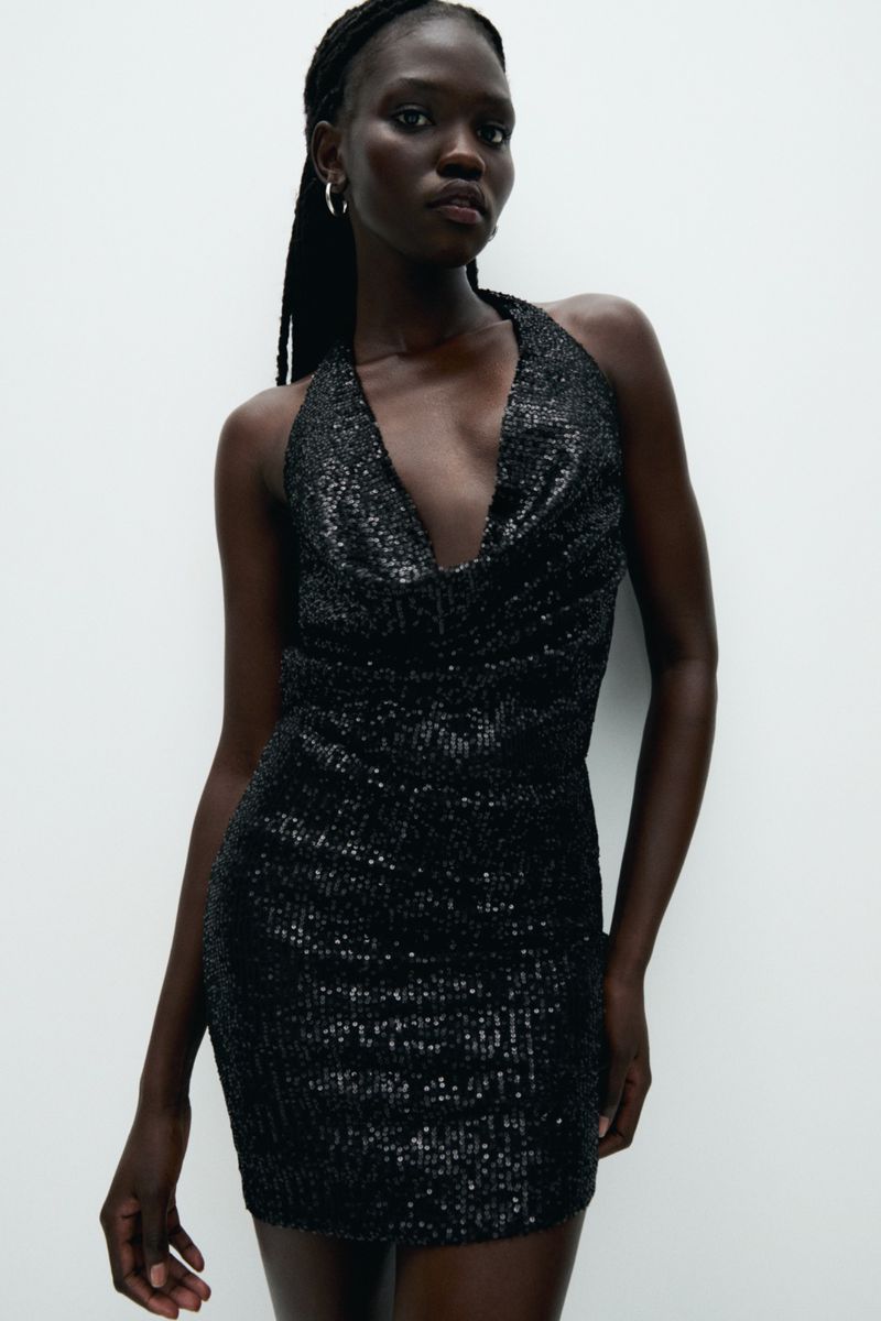Model Anok Marial wearing a black sequin halter dress against a plain white seamless studio background.
