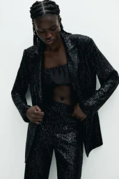 Model Anok Marial wearing a black sequin blazer and matching trousers for Pull & Bear shot by Louie Cobo against a seamless white backdrop.