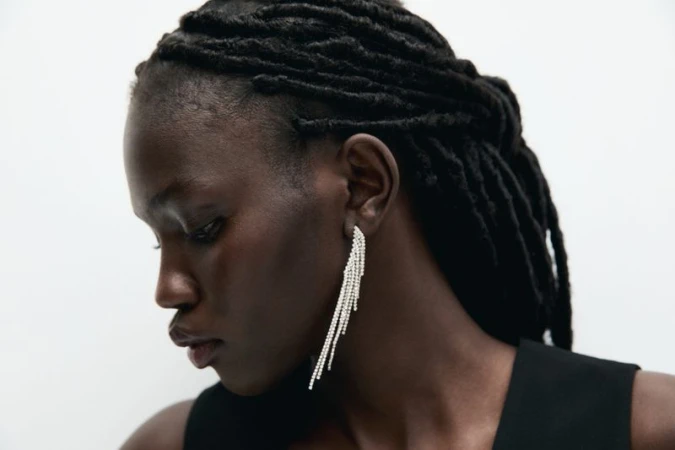 Close-up portrait of model Anok Marial wearing rhinestone fringe earrings against a plain white background