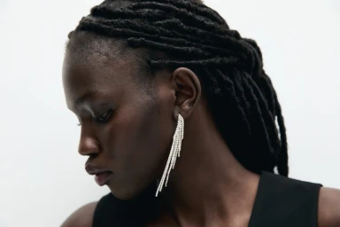 Close-up portrait of model Anok Marial wearing rhinestone fringe earrings against a plain white background