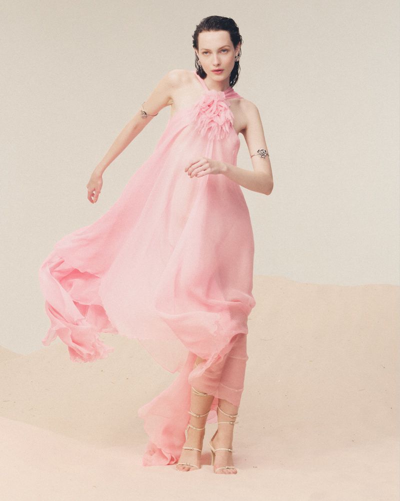 Fashion model in a flowing pink gown poses in a studio with soft lighting, showcasing airy elegance and a dreamy aesthetic.
