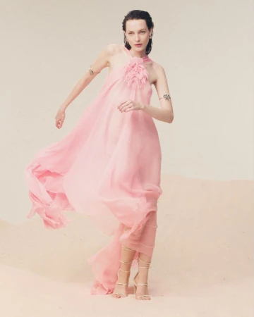 Fashion model in a flowing pink gown poses in a studio with soft lighting, showcasing airy elegance and a dreamy aesthetic.