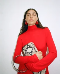 Model wearing a bright red turtleneck and holding a snakeskin print handbag against a white background for Net-A-Porter