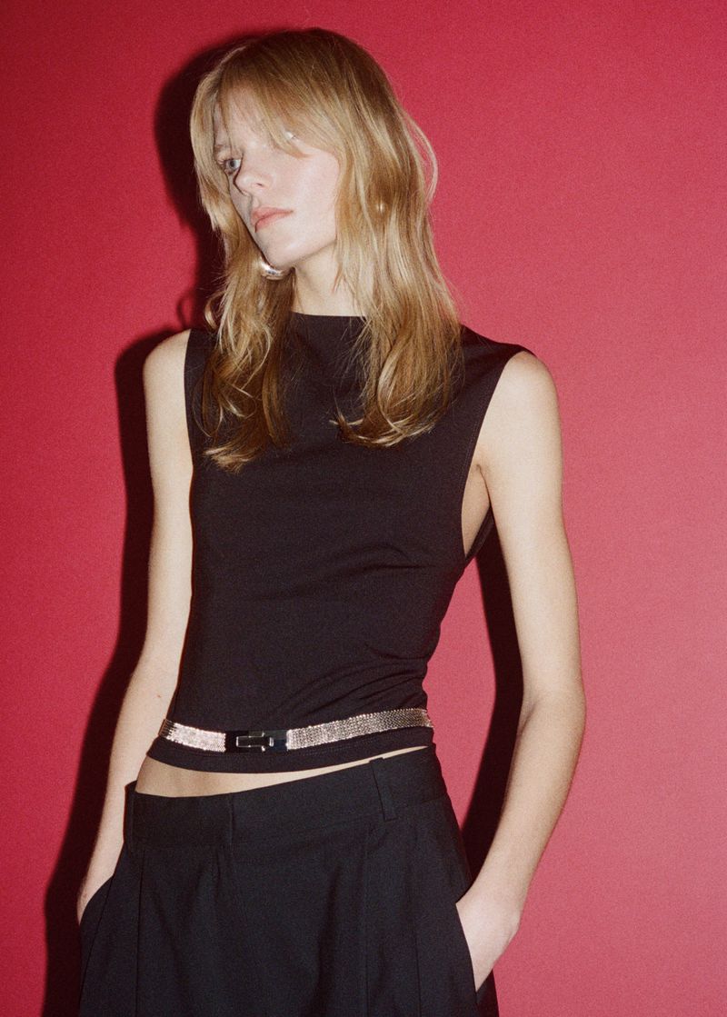 Model wearing a black top and trousers with a metallic belt against a red background