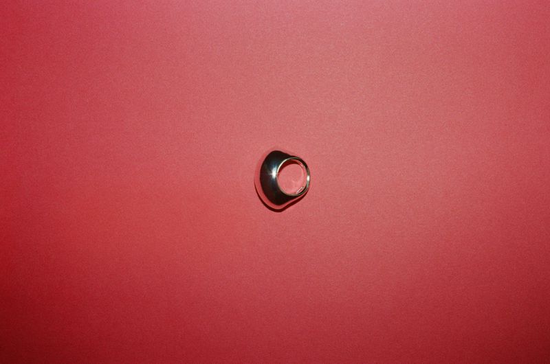 Studio shot of a metallic ring on a red background with soft lighting and a minimalist composition.