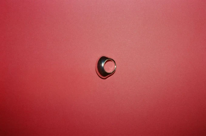 Studio shot of a metallic ring on a red background with soft lighting and a minimalist composition.
