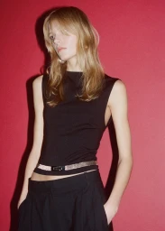 Model wearing a black top and trousers with a metallic belt against a red background
