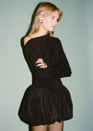 Model with blonde hair wearing a black long-sleeve dress and silver earrings against a muted green backdrop for Mango.
