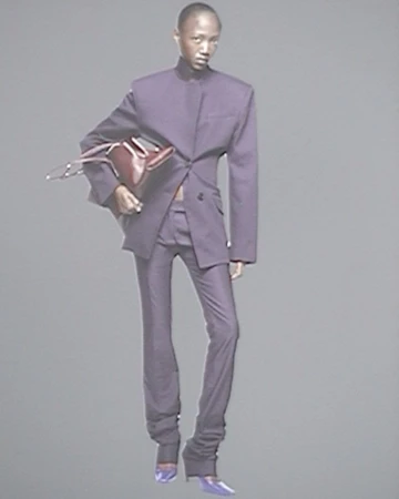 Fashion photo of a Black model in a purple suit holding a brown purse, set against a neutral background in a studio environment.
