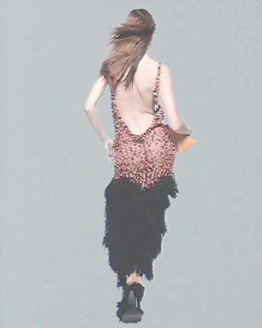 Runway fashion show: A woman walks away wearing a sparkling pink mini dress with a feathered black skirt, high heels, and a clutch.
