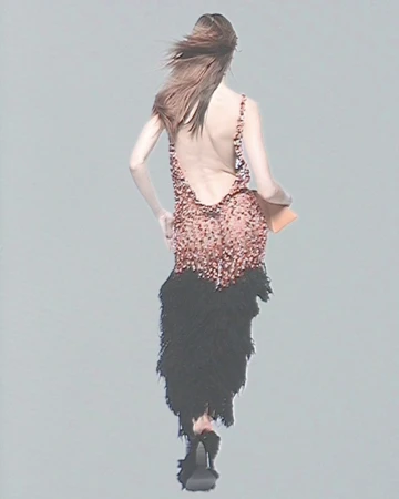 Runway fashion show: A woman walks away wearing a sparkling pink mini dress with a feathered black skirt, high heels, and a clutch.