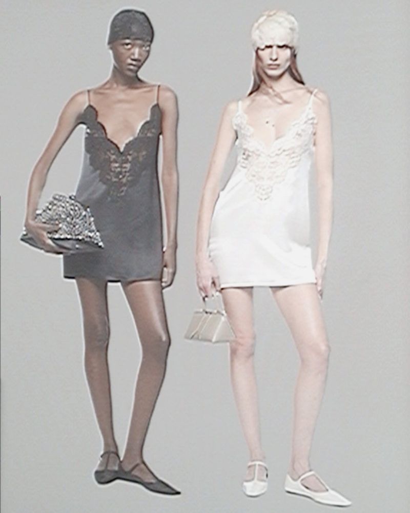 Two female models posing in mini slip dresses against a grey background for The Attico S/S 25 collection.