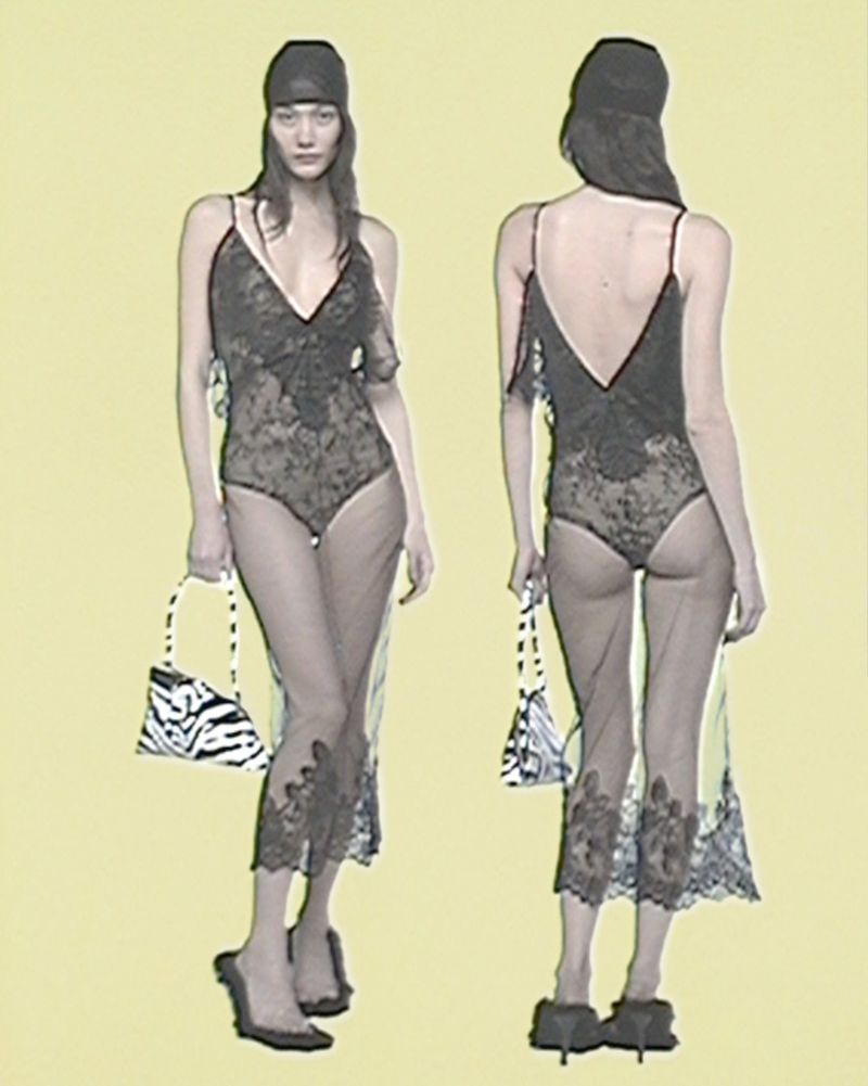Fashion shot of a woman in a black lace bodysuit with a sheer dress, holding a zebra-striped purse, in front of a pale yellow background.