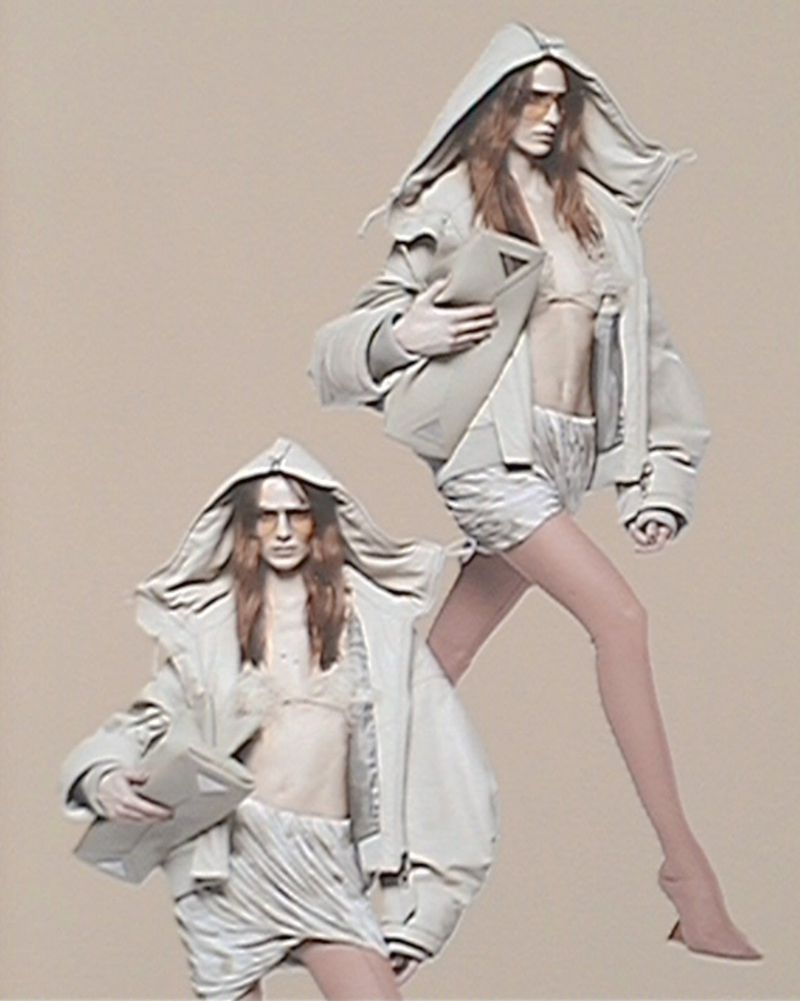 Two fashion models in oversized hooded jackets pose in a studio setting, presenting avant-garde style against a neutral background.