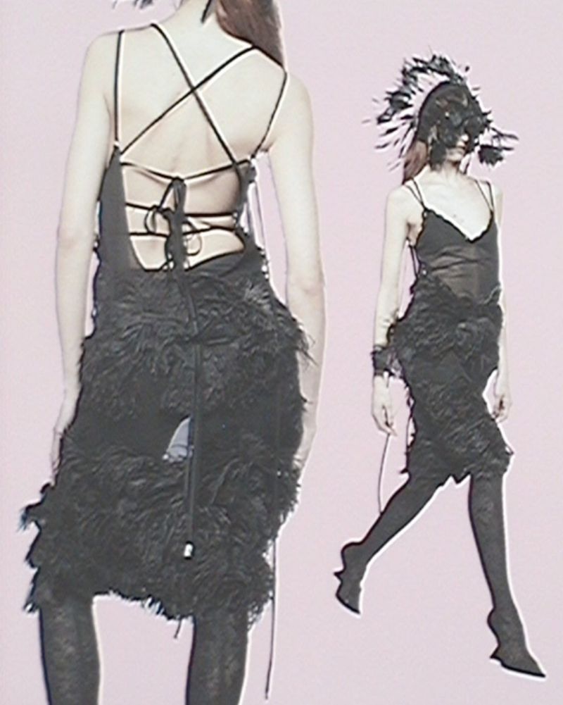 Two women showcasing fashion forward black dresses with feather accents and unique headwear against a light pink background in a studio shot.
