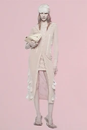 Model wearing a long buttoned beige cardigan and white headwrap holding a clutch against a pink backdrop