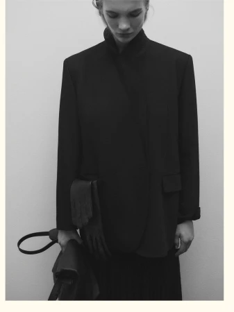 Model wearing a black structured blazer and holding a handbag against a neutral background