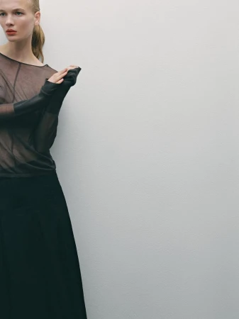 Model in sheer brown top and black skirt posing against a plain grey studio backdrop for Massimo Dutti