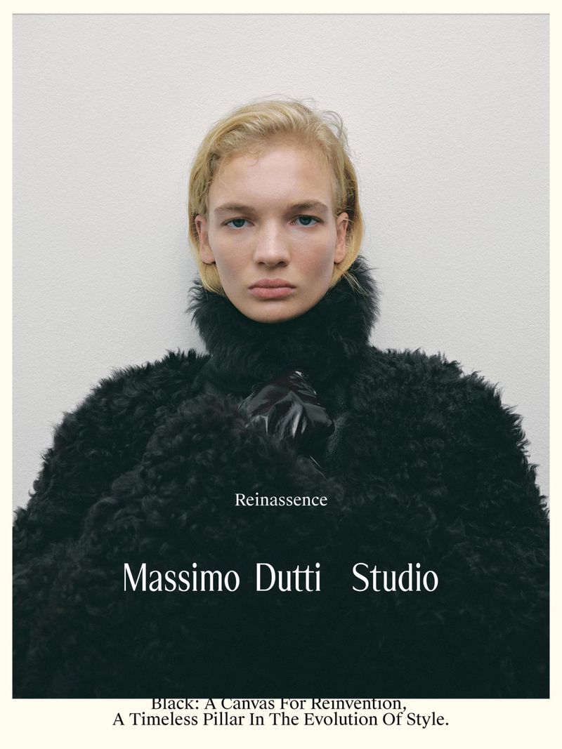 Fashion portrait of a fair-skinned woman with blonde hair wearing a black textured coat against a light neutral background.