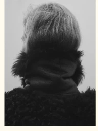 Rear view portrait of a person wearing a textured dark fur collar coat against a plain background