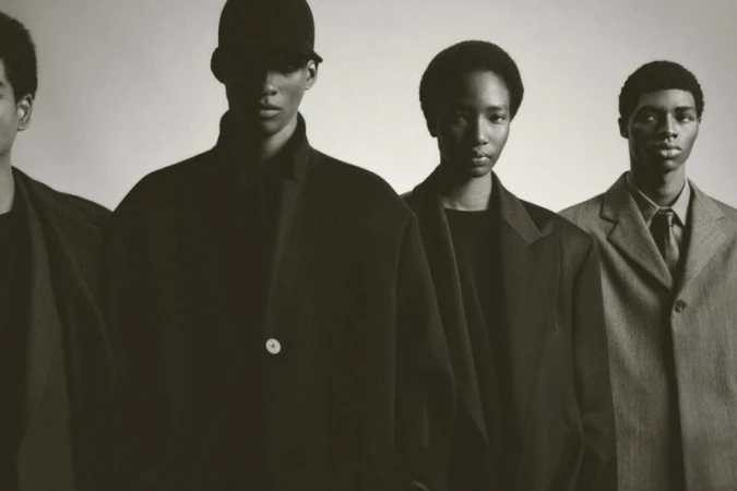 Four African American men stand in a row, wearing black and gray suits against a grey background, photographed in a studio setting.