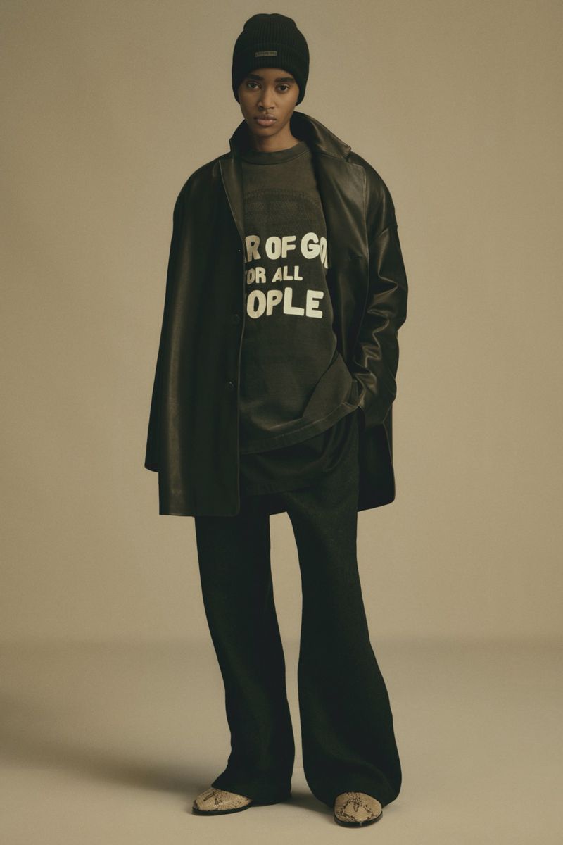 Fashion model posing in a black coat, pants, and beanie against a neutral backdrop. A trendy, editorial style for Visie.