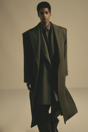 Man wearing a structured grey wool overcoat and suit jacket against a neutral studio background.