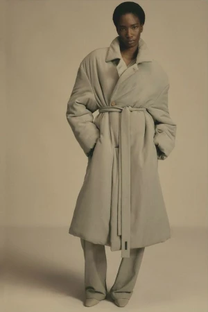 Model wearing an oversized beige puffer coat with a matching tie belt against a neutral background
