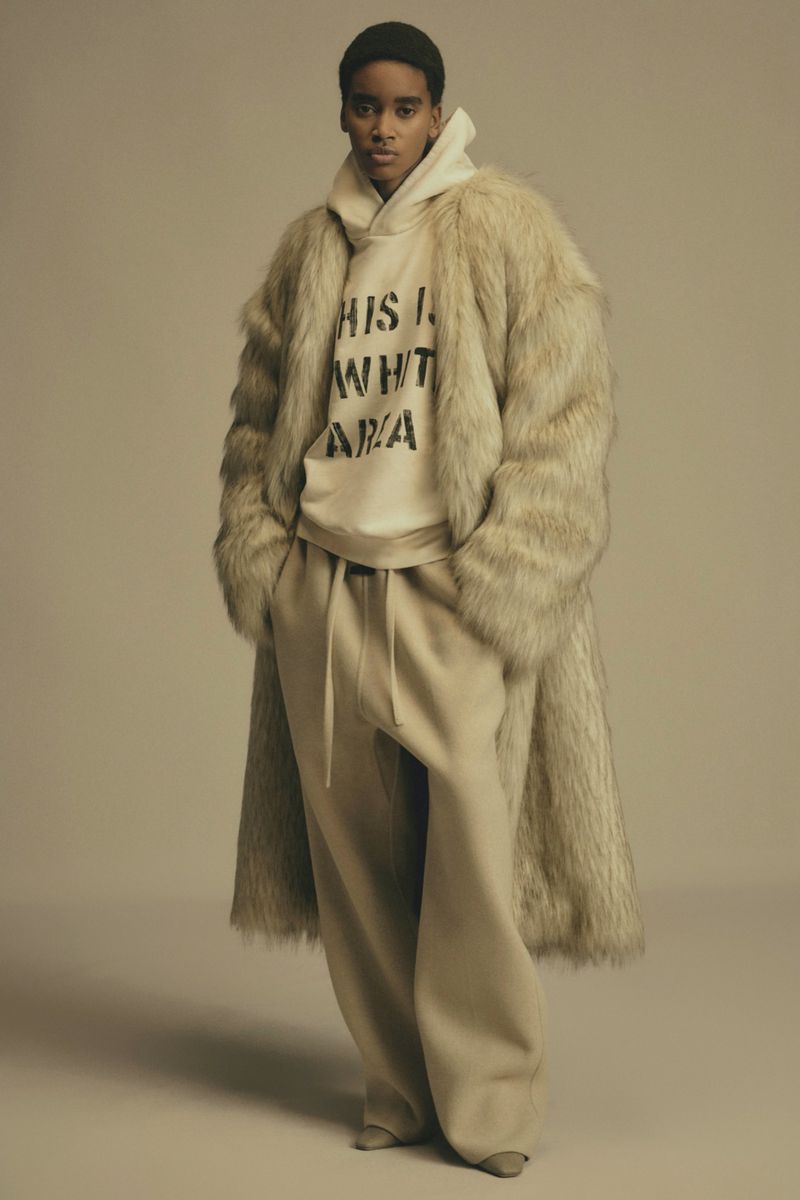 Fashion portrait of a young adult, wearing a faux fur coat and hoodie, set against a neutral studio backdrop, showcasing modern style.