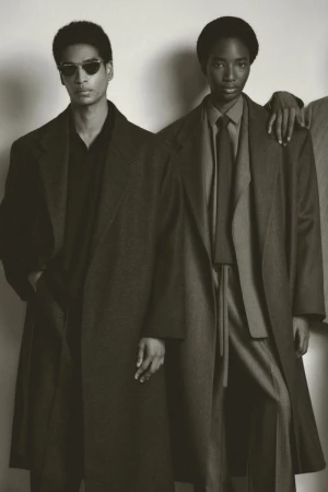 Two models wearing tailored oversized coats and sunglasses against a plain studio background.